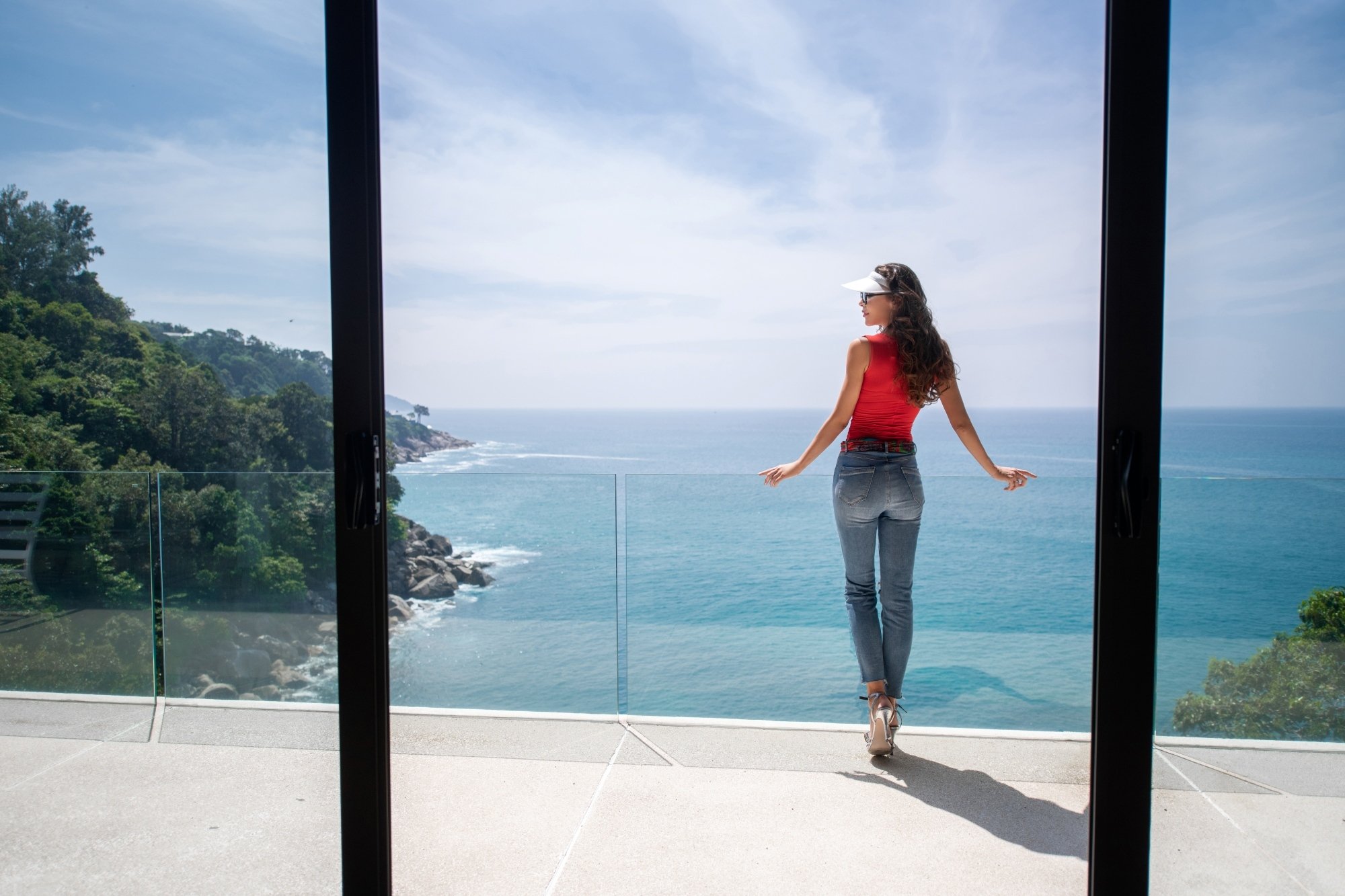 Hermosa mujer en jeans apreciando de juna vista espectacular al mar desde el balcon