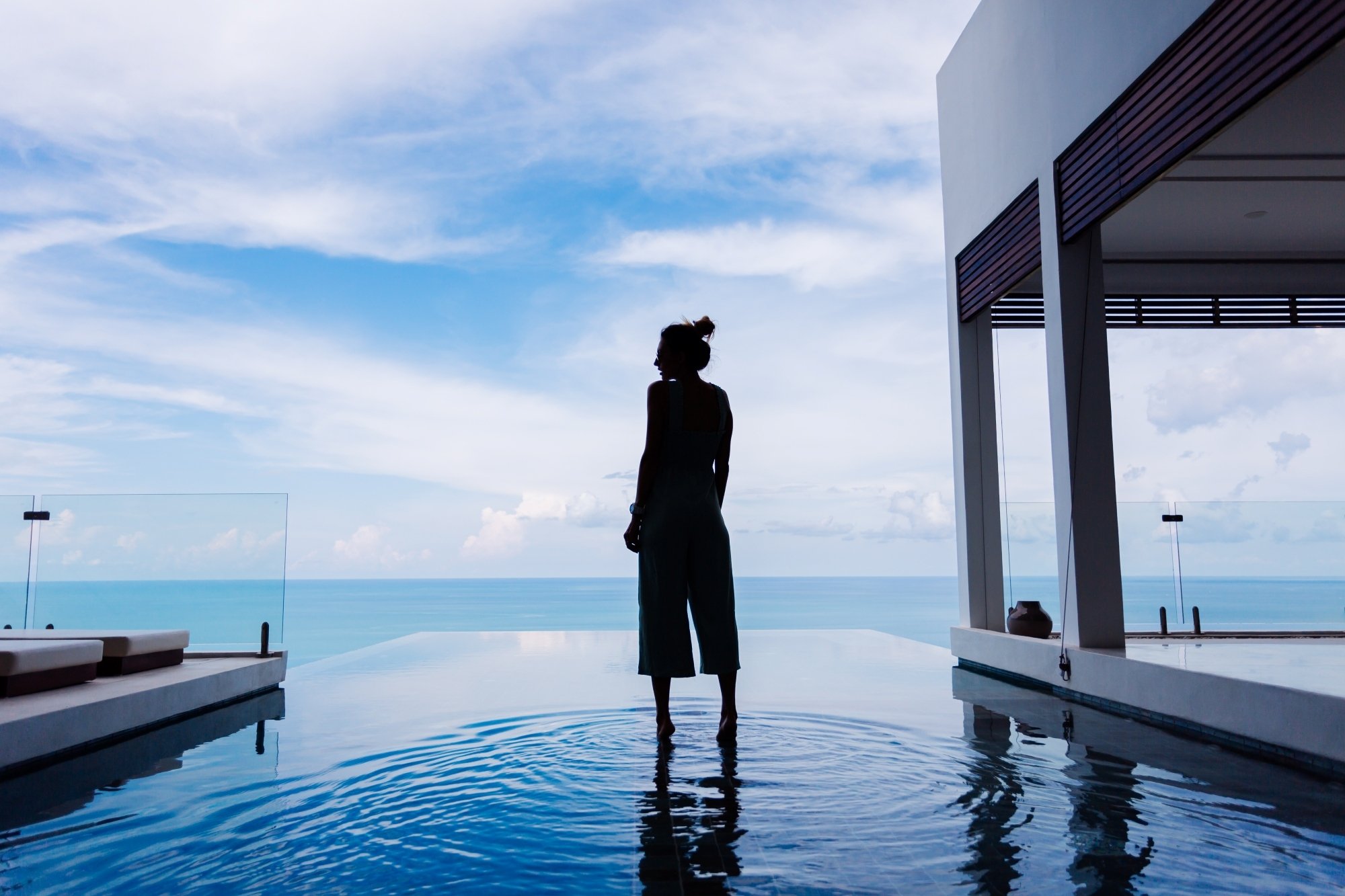 Silueta de una mujer caminando sobre la superficie del agua de la piscina infinity, disfrutando la espectacular vista al mar